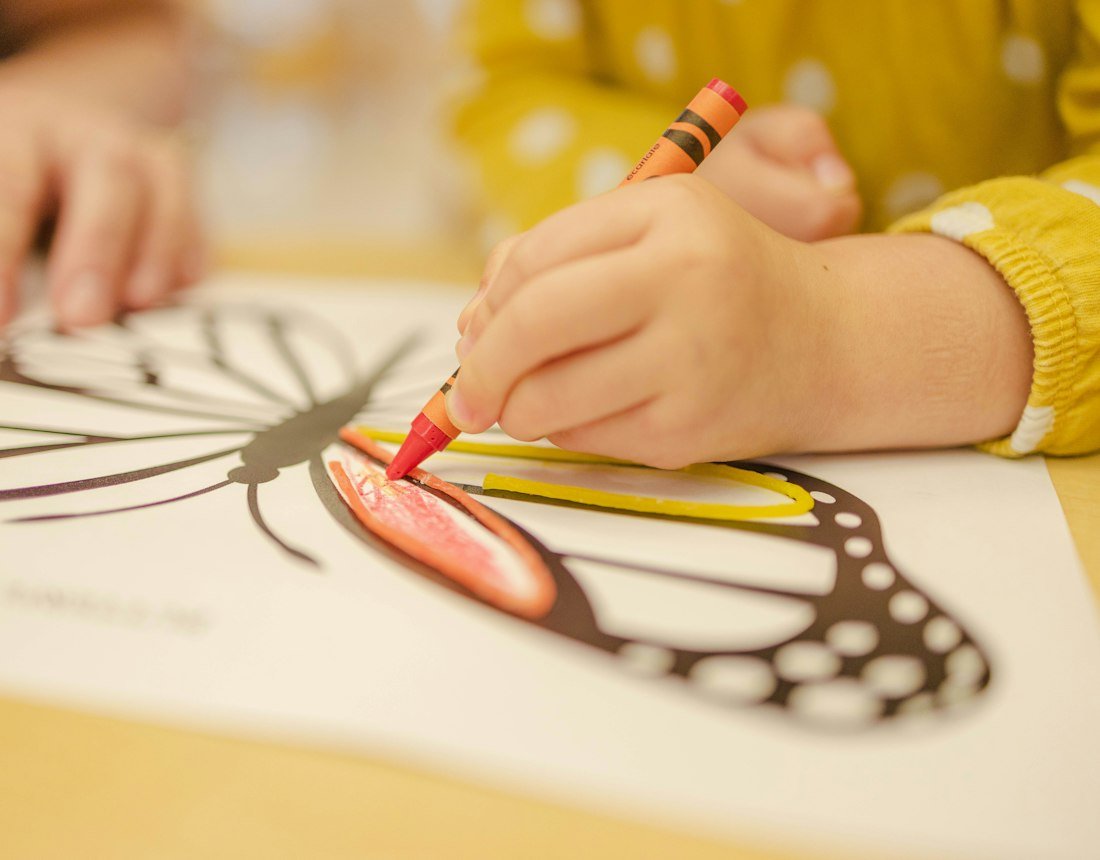 A child colouring a butterfly drawing with a crayon