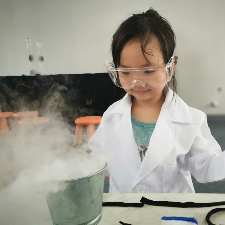 A child in a lab coat and safety goggles watching an experiment