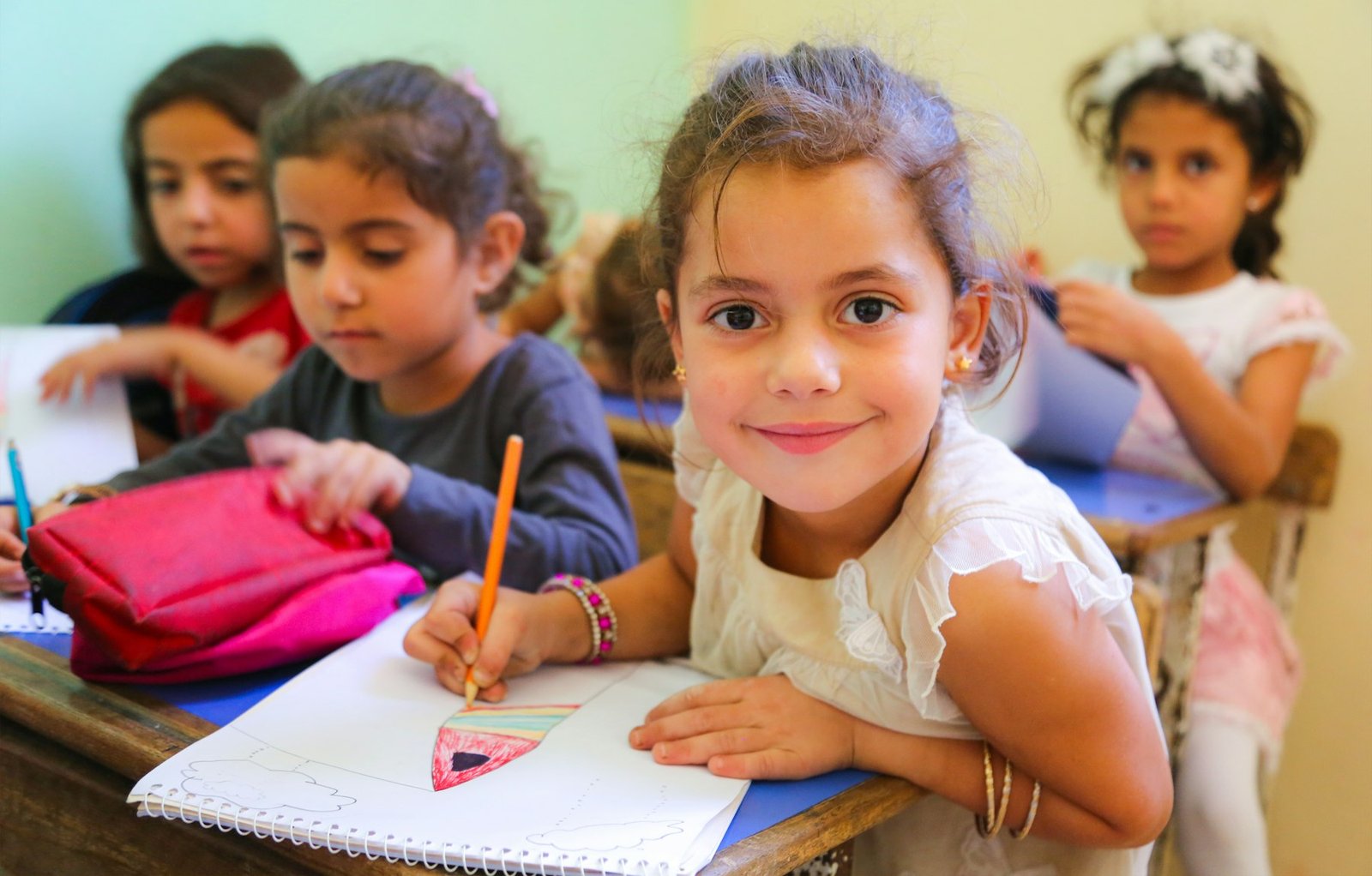 A smiling girl drawing with a pencil at her desk in a classroom