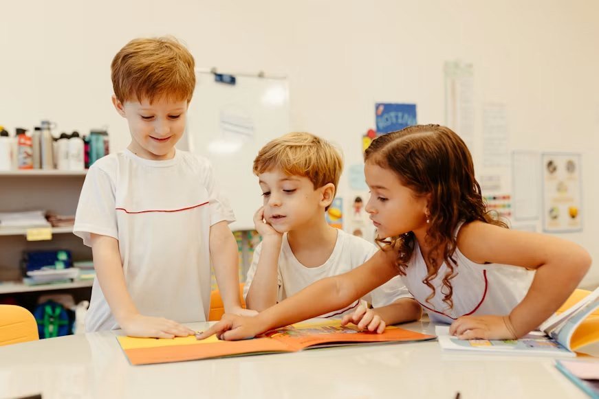 Three children reading a picture book together at a classroom table